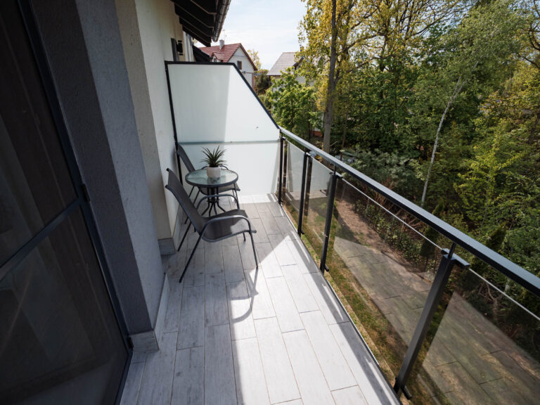 Balkon z miejscem do wypoczynku, stolikiem, krzesłami i widokiem na zieleń
